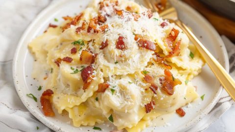 Creamy and cheesy ravioli carbonara with bacon bits served in a white plate.