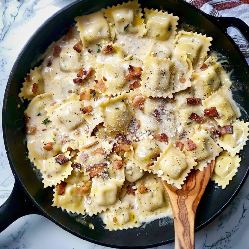 Ravioli pasta in carbonara sauce in a skillet, top view.