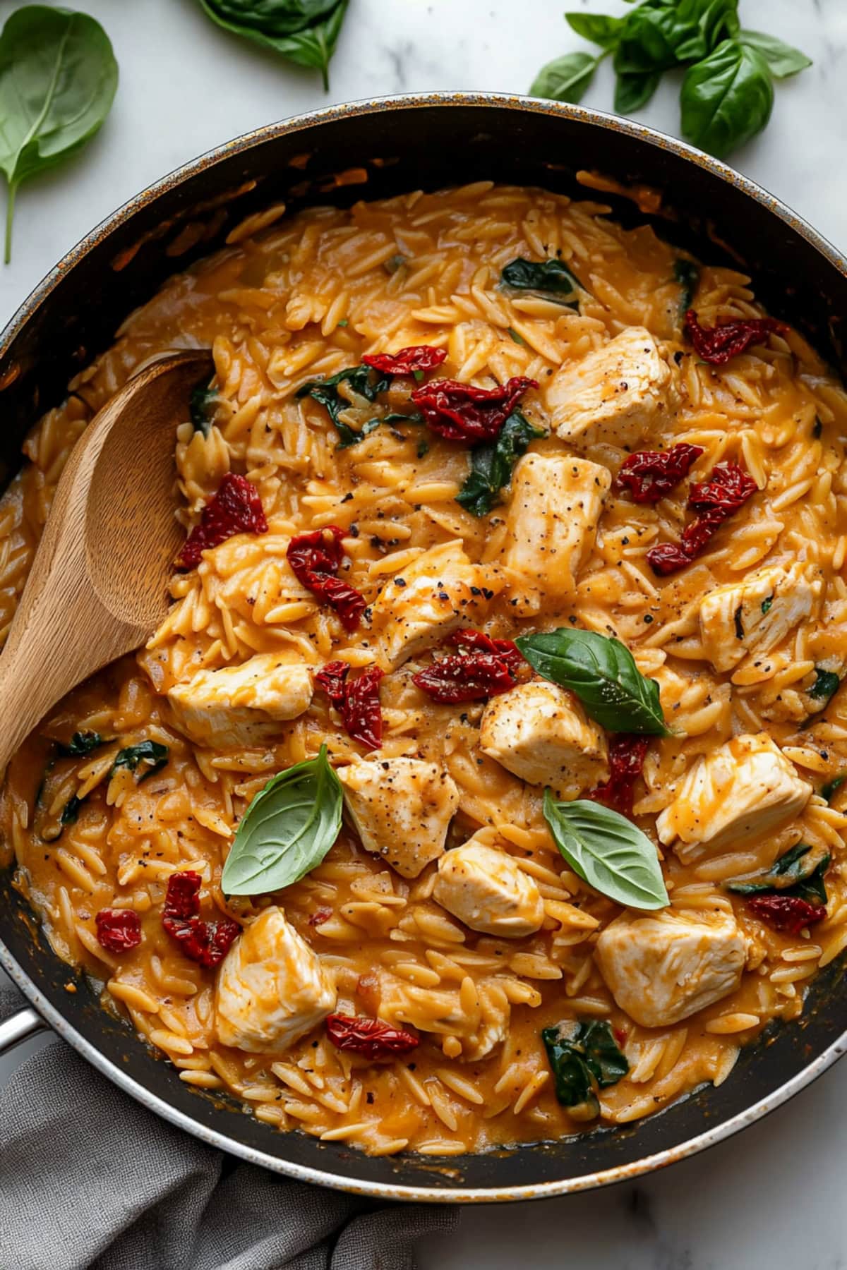 One-pan marry me chicken orzo with sun-dried tomatoes, baby spinach, and fresh basil, overhead view.