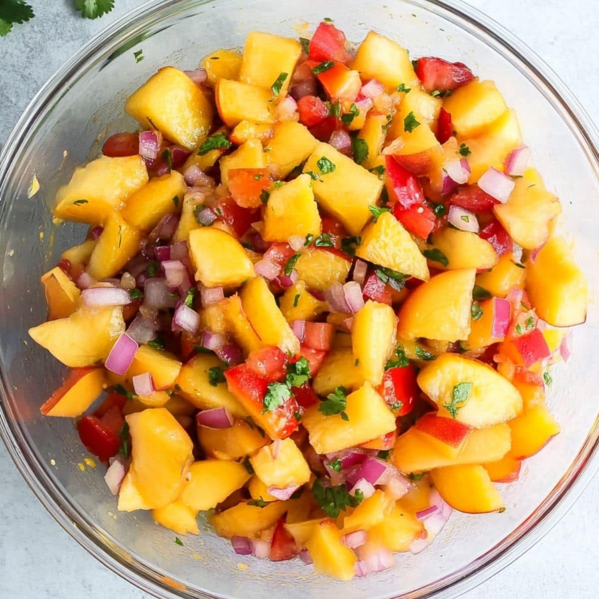 Diced peaches, red bell pepper, red onion, and jalapeño in a glass mixing bowl.