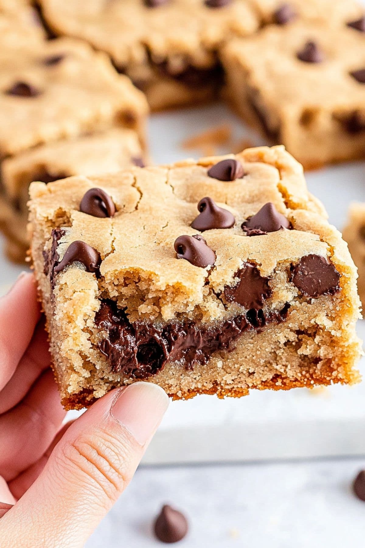 Hand holding a piece of peanut butter chocolate chip cookie bar.