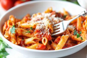 Penne arrabbiatta serving in a white bowl garnished with grated parmesan cheese.