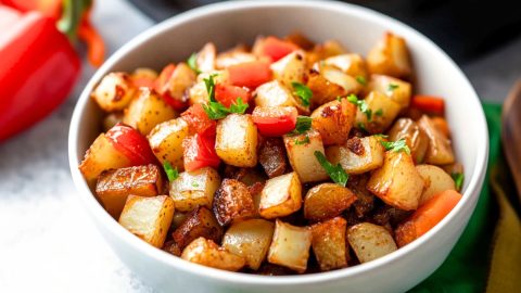 White bowl with a serving of diced potatoes with chopped bell peppers and onions.