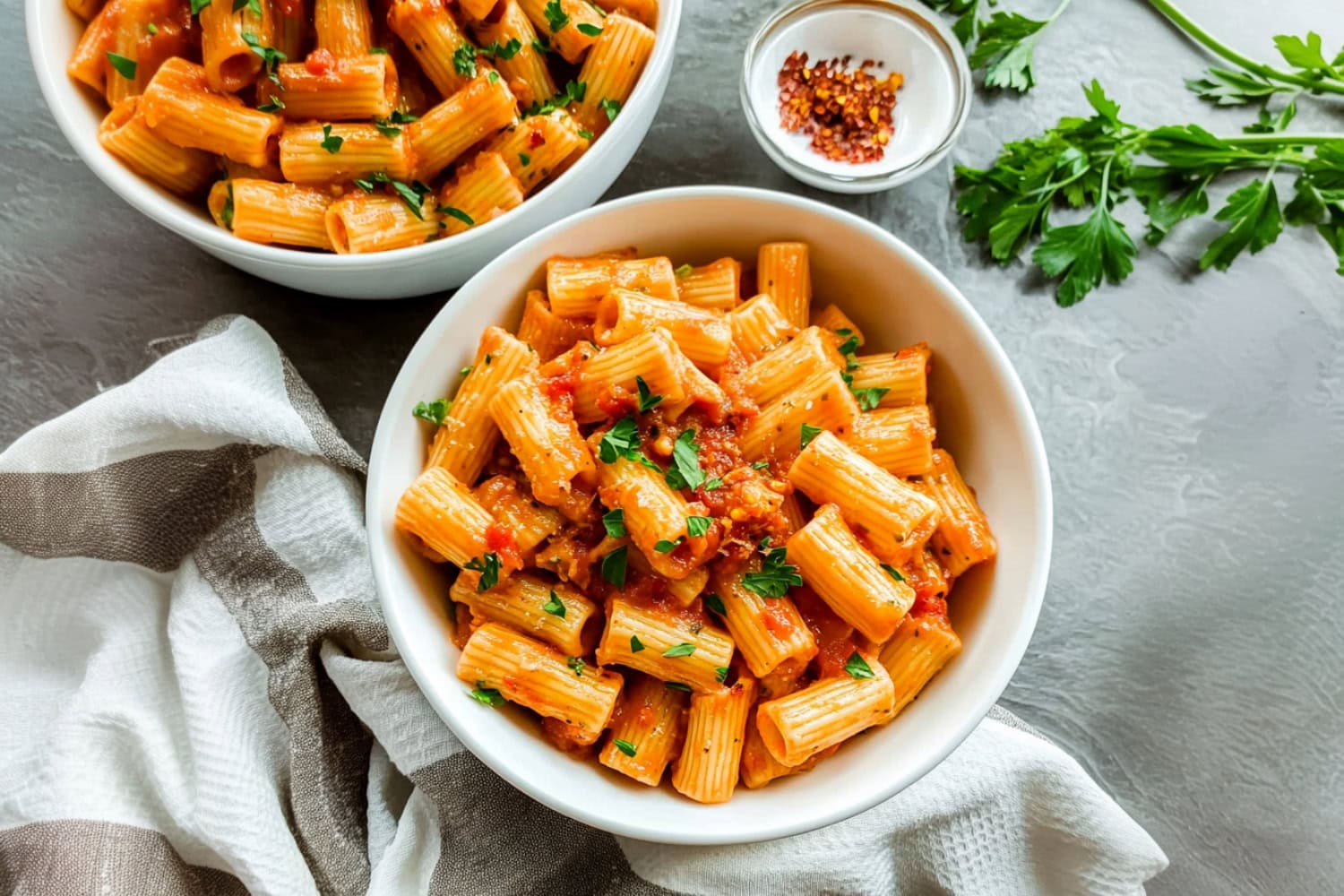 Homemade rigatoni arrabbiata served in bowls, with chopped parsley and red pepper flakes.