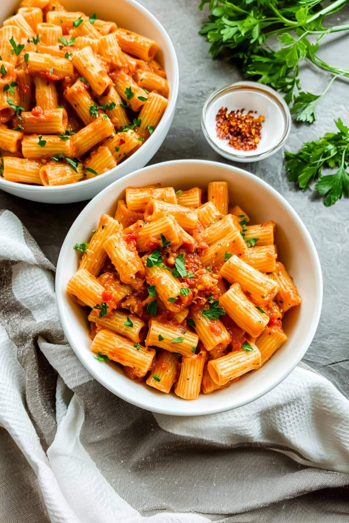 Two bowls of rigatoni arrabbiata in a bowl, garnished with pepper flakes.