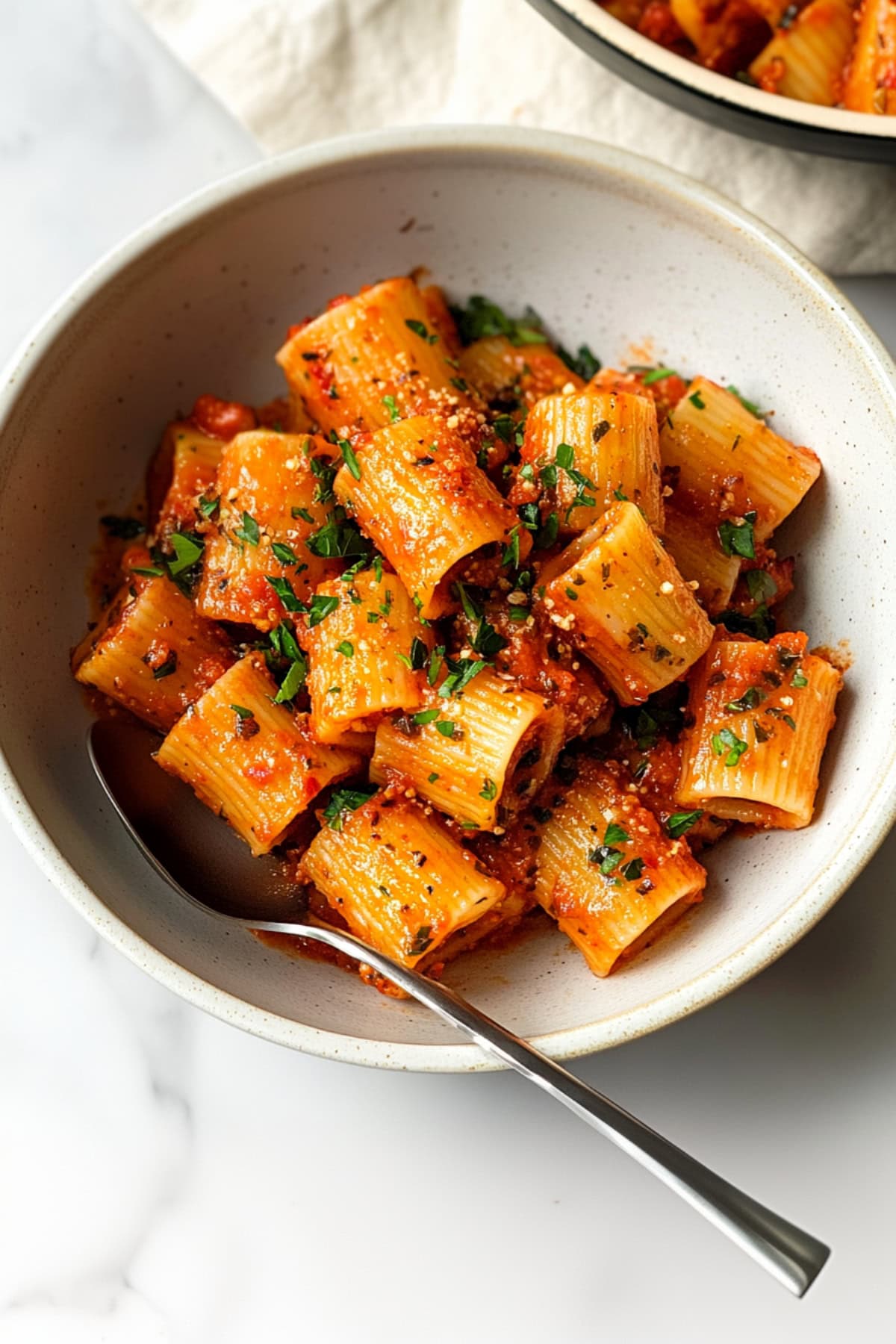 An overhead view of rigatoni arrabbiata in a bowl with red pepper flakes and chopped parsley.