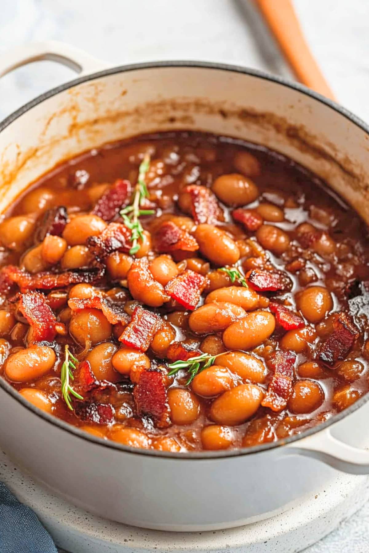 White Dutch oven pot with baked beans cooked in savory sauce with bacon.