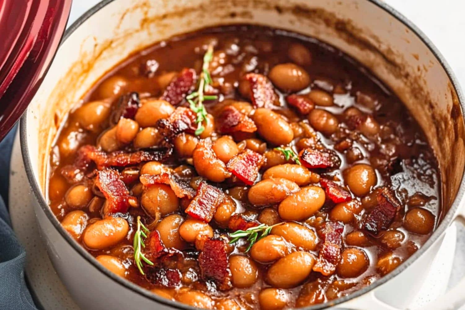 White Dutch oven with baked beans cooked in savory sauce and chopped bacon.