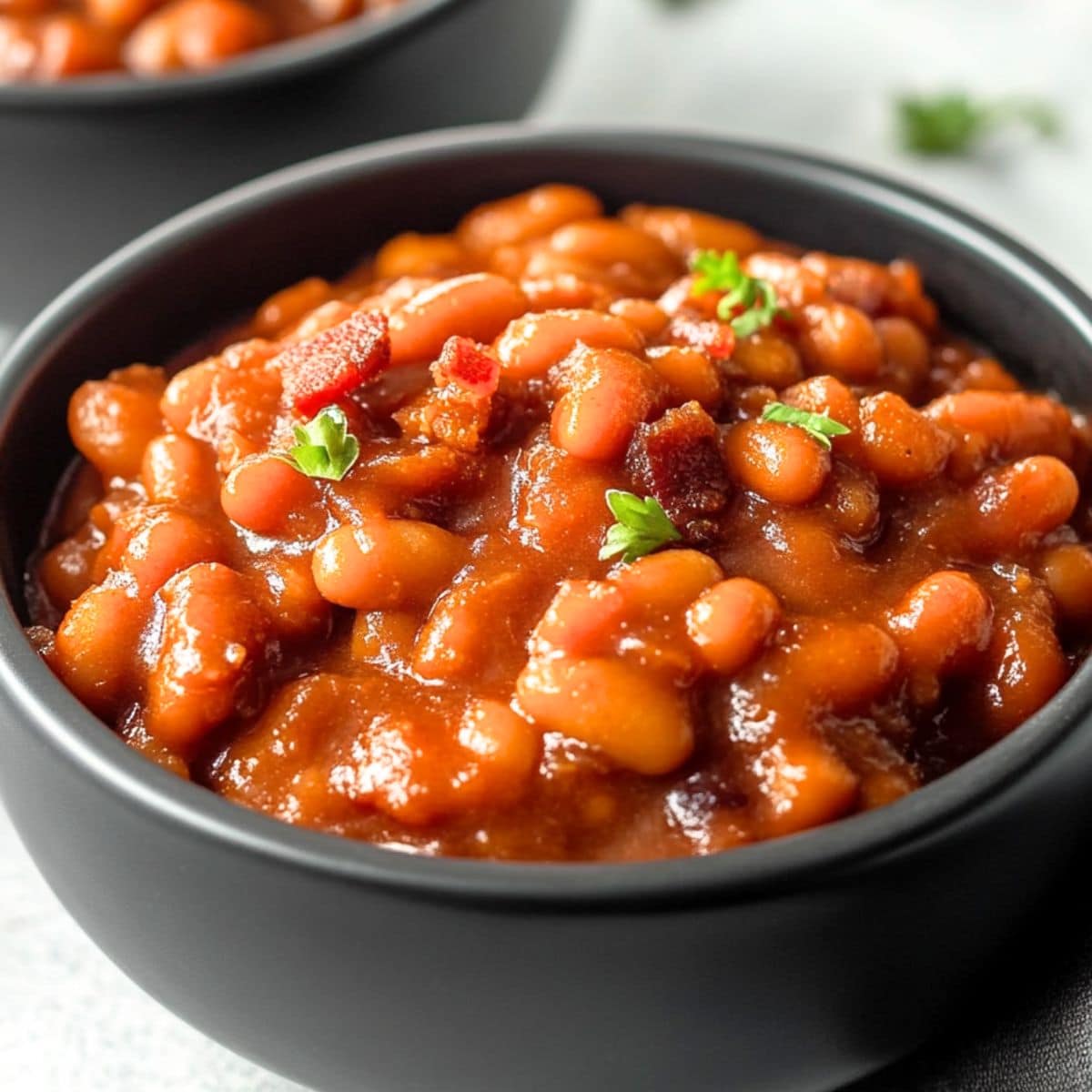 Serving of root beer baked beans in two black bowls.