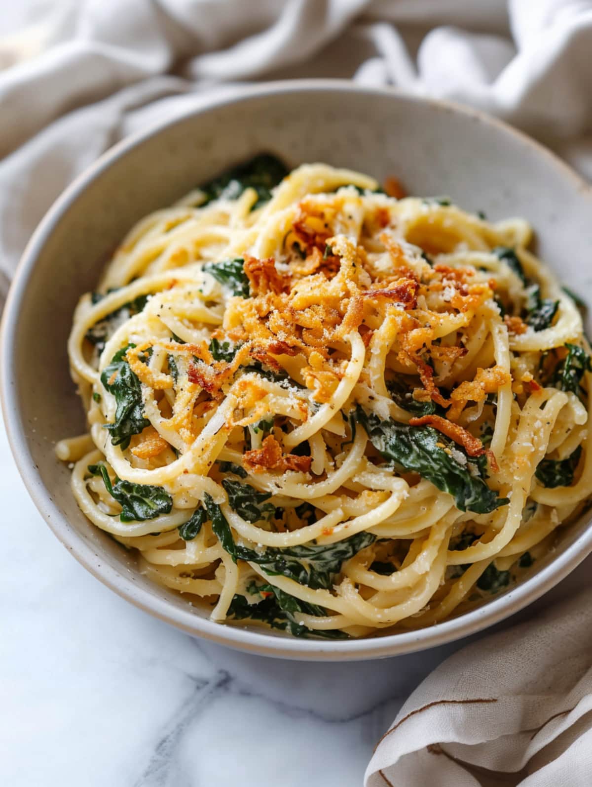 Close-up of Monterey spaghetti, with tender pasta, crispy onions and spinach, coated in a sauce.