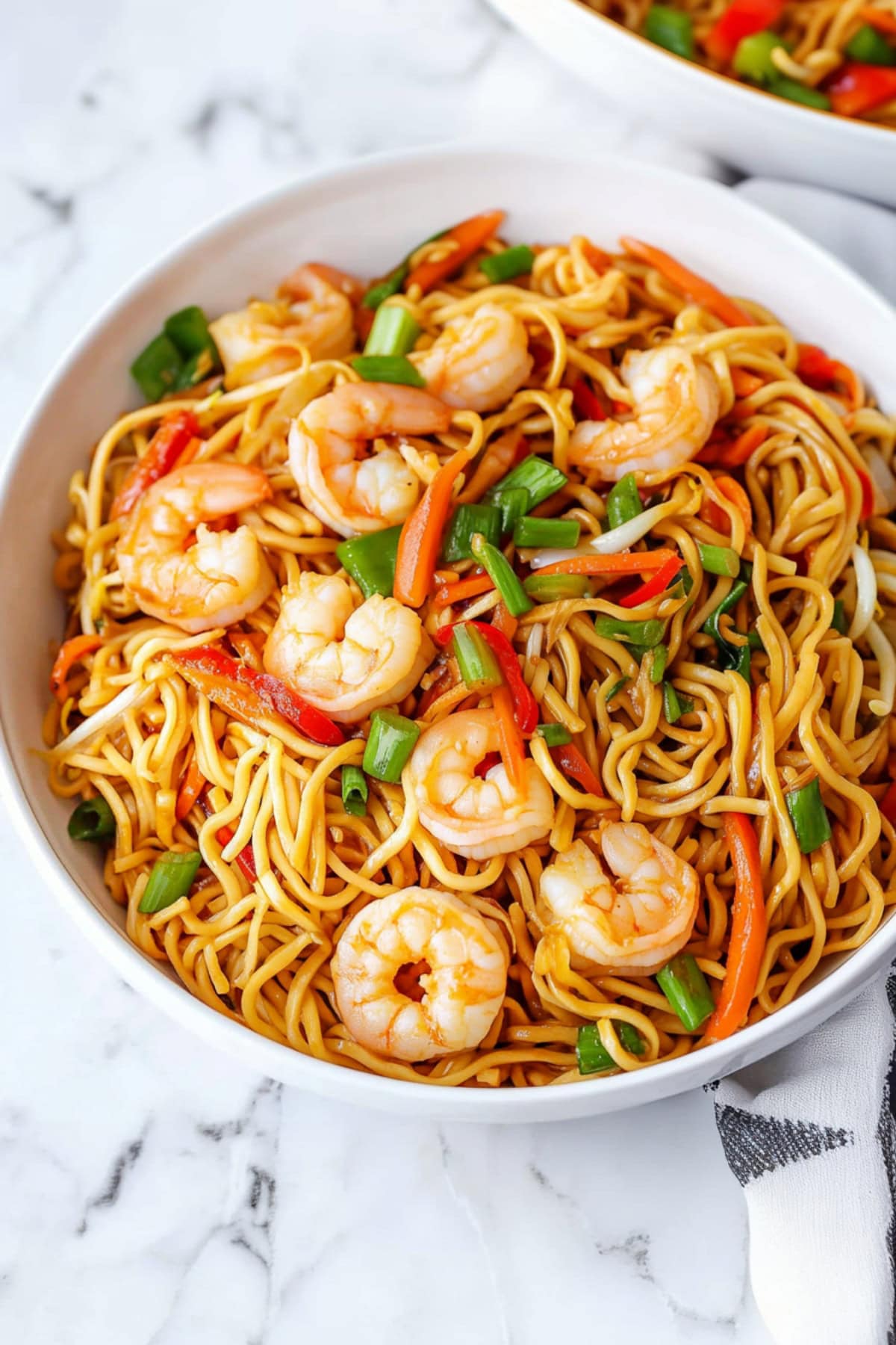 Shrimp chow mein noodles with bell peppers, carrots, bean sprouts, garnished with green onions in a bowl.