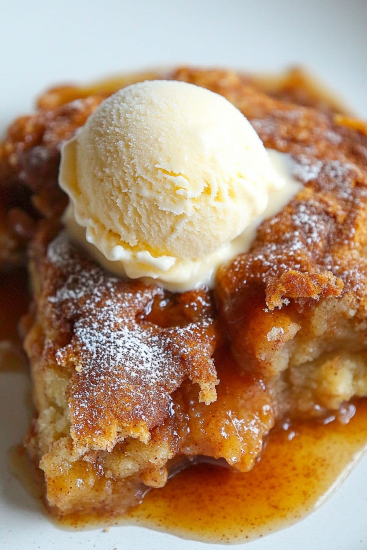 Serving of snickerdoodle cobbler served in a white plate with a scoop of vanilla ice cream on top.