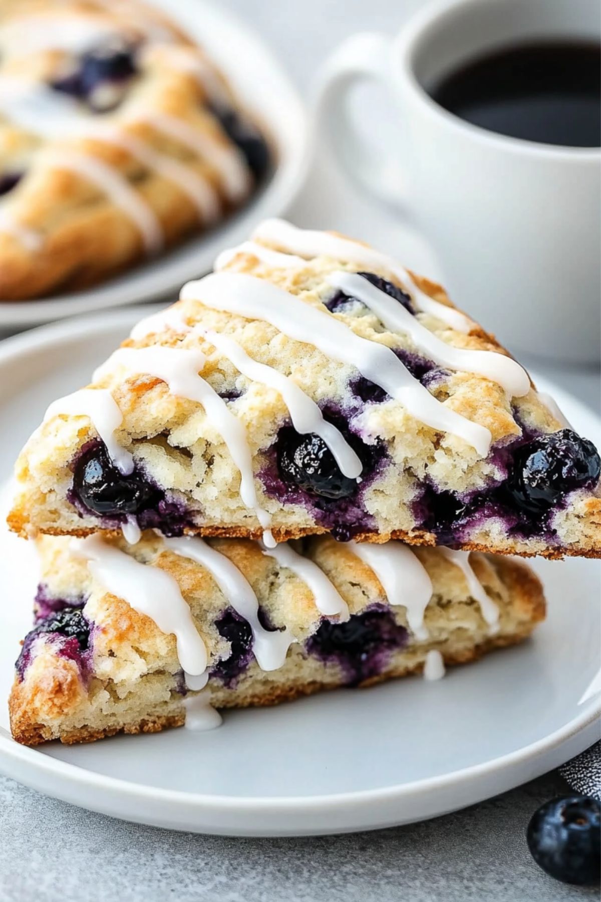 Two Starbucks blueberry scones with a drizzle of white glaze served on a white plate with a cup of coffee on the side.