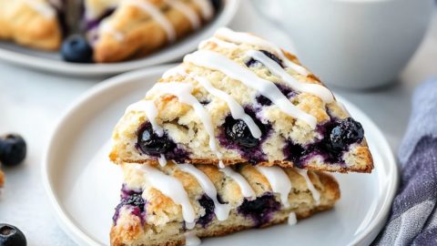 Two servings of blueberry scones with drizzle of sugar glaze served in white plate with cup of coffee on the side.