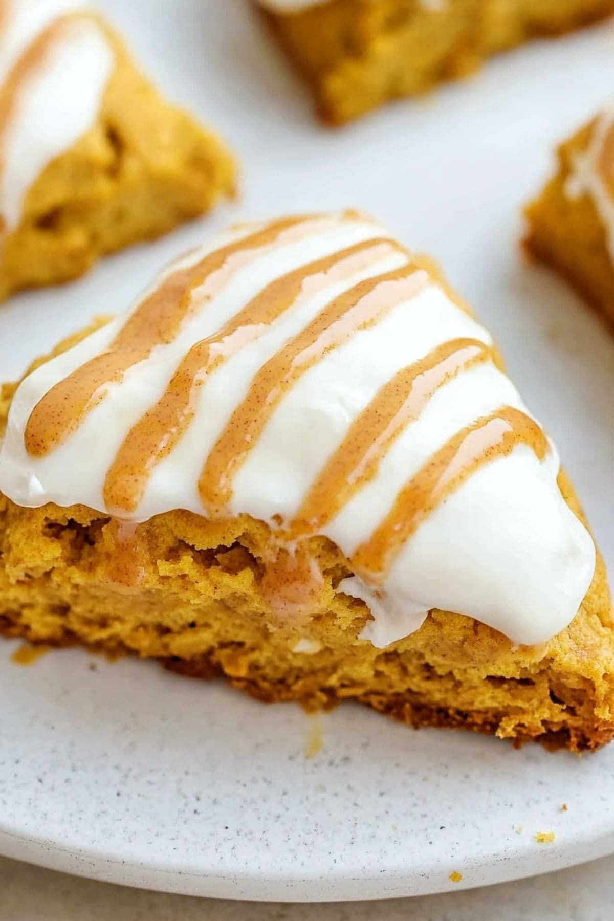 Pumpkin scone with white and spiced glaze on a white table, close up.