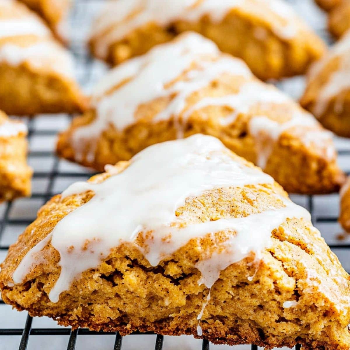 Pumpkin scones with white glaze on a cooling rack.