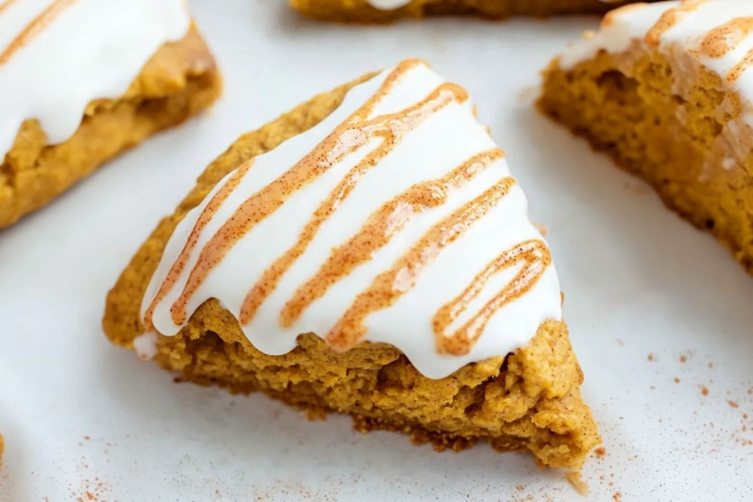 Starbucks pumpkin scones with white glaze drizzled with spice glass sitting on a white surface.