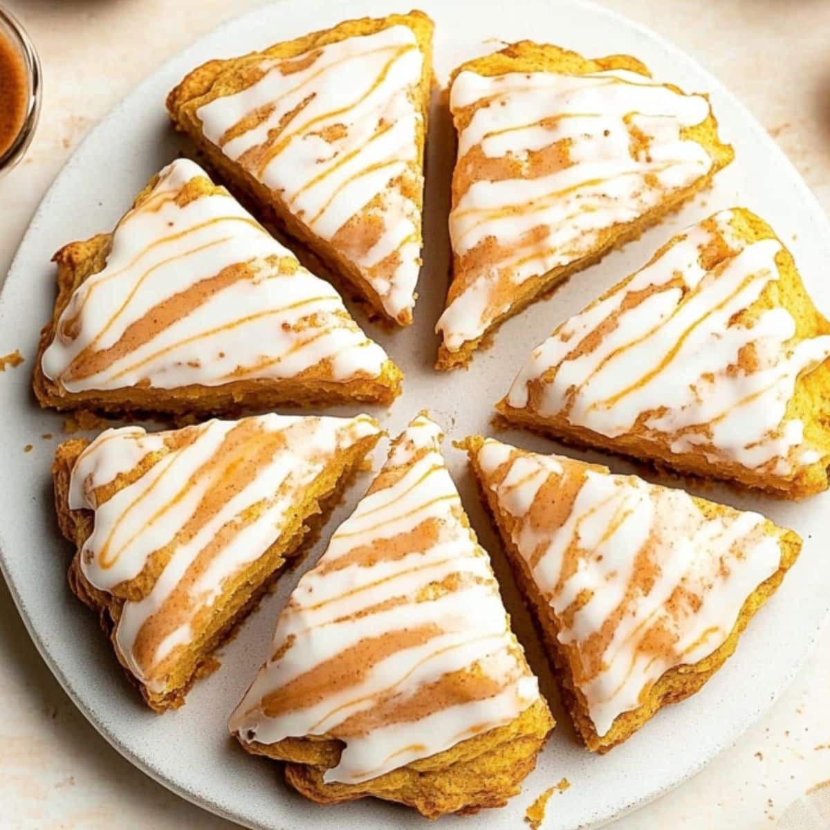 Pumpkin scones covered with white glaze drizzled with spice glaze served in a white plate.