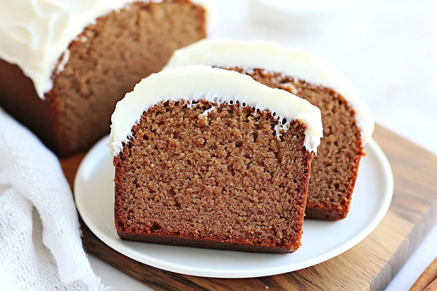 Whole and sliced gingerbread loaf bread in a white plate sitting on top of wooden board.