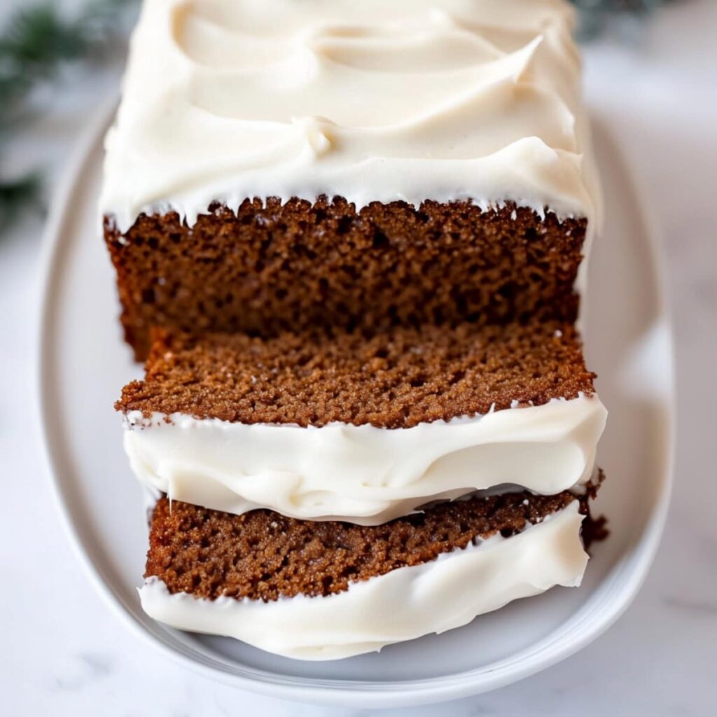 Sliced whole gingerbread loaf bread with cream frosting on top served in a white plate.