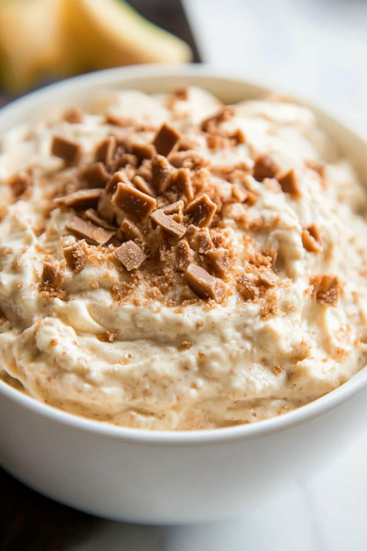 Creamy toffee dip served in a white bowl garnished with chopped toffee bits on top.