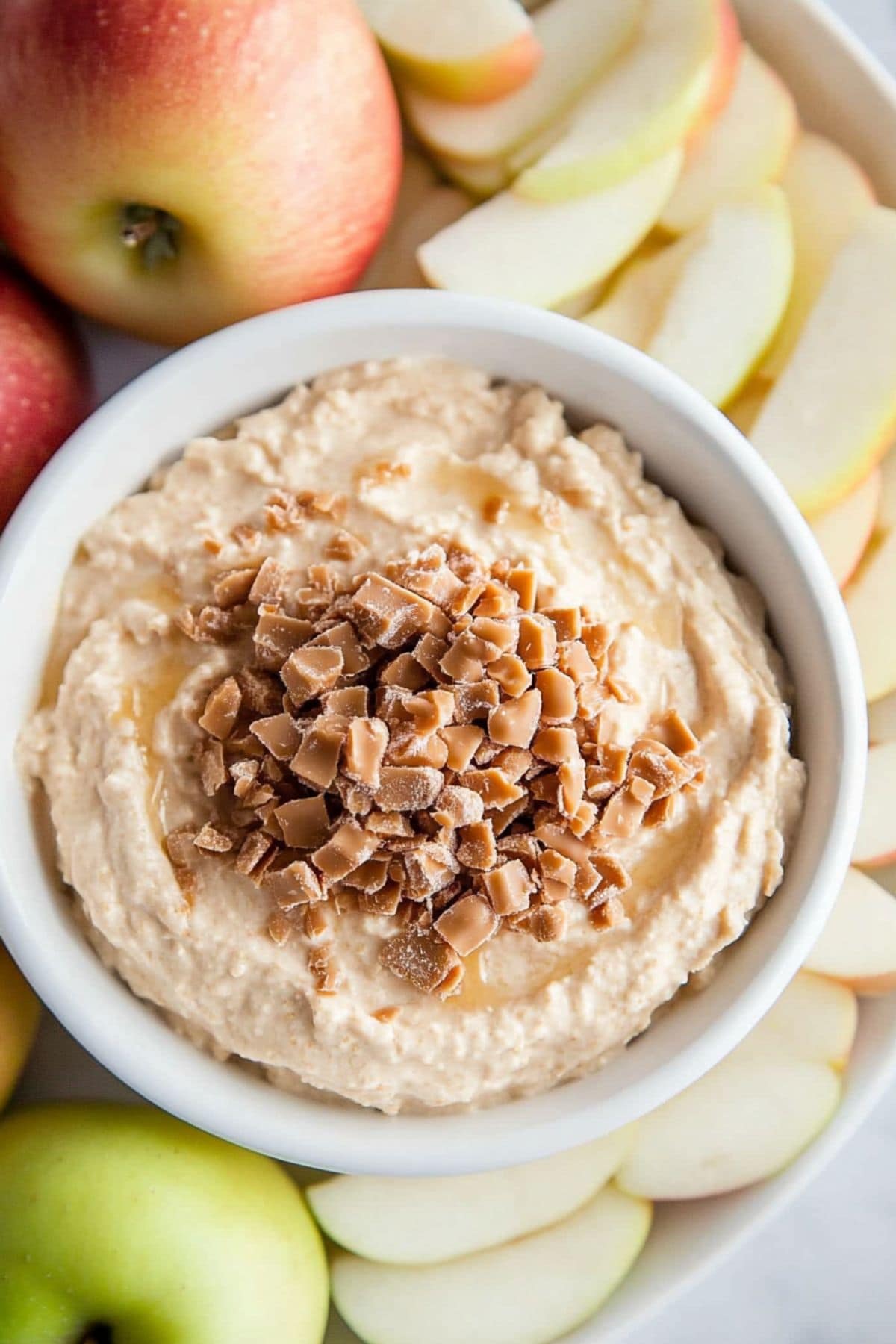 Cream dip with toffee bits served in a bowl with a platter of sliced apples.