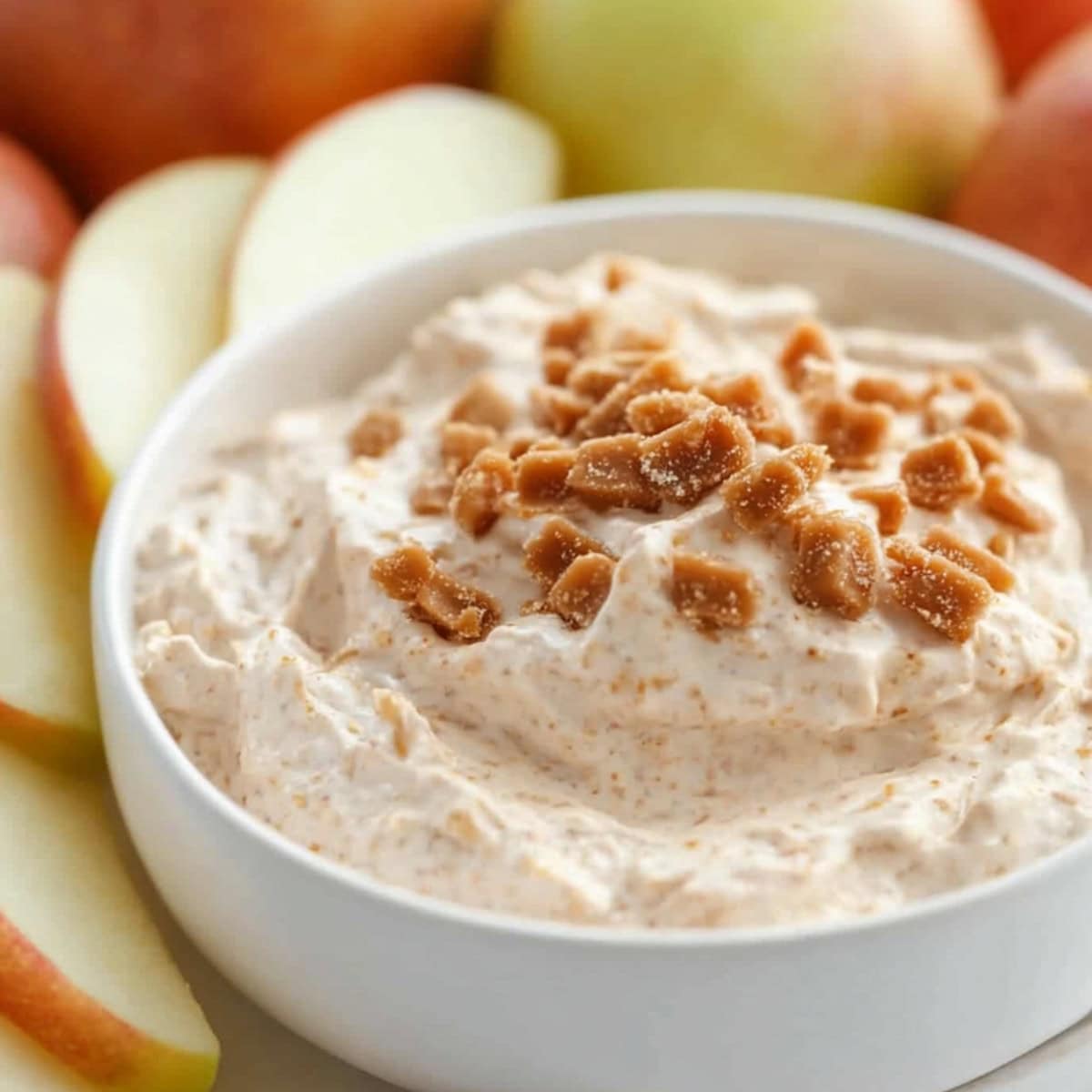 Creamy toffee dip in a white bowl garnished with chopped toffee bits.