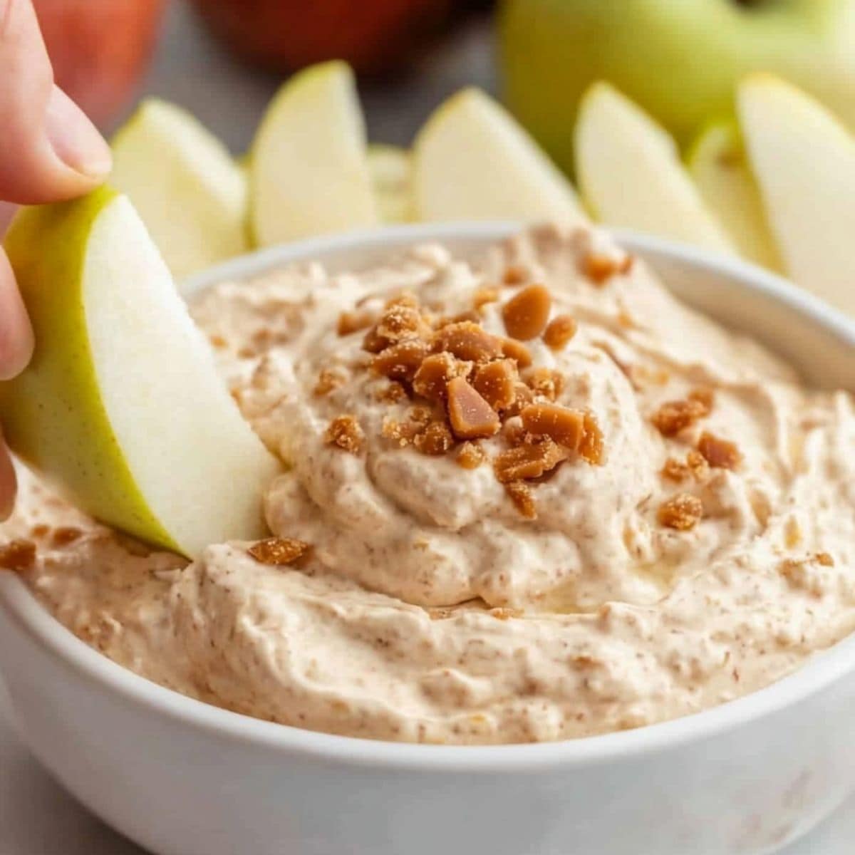 Hand holding an apple slice dipping it to a bowl of creamy toffee dip. 