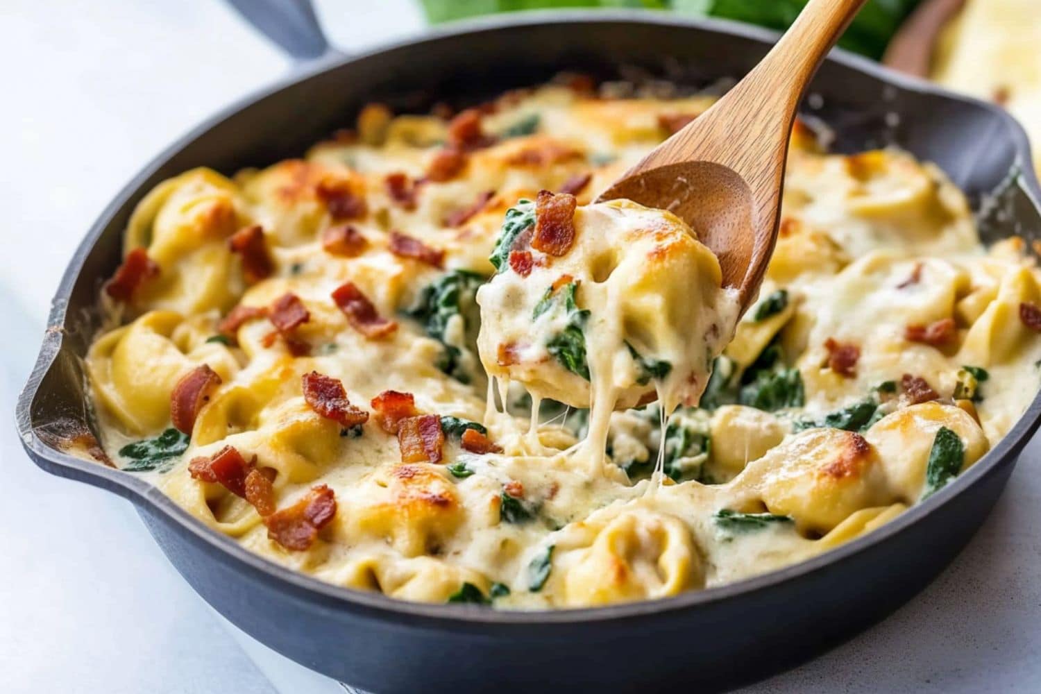 Tortellini pasta cooked in creamy sauce, chopped bacon and spinach in a skillet pan.