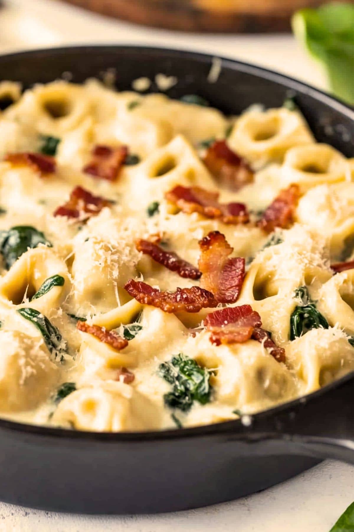 Skillet pan with cheesy tortellini cooked in creamy pasta, chopped bacon and spinach.