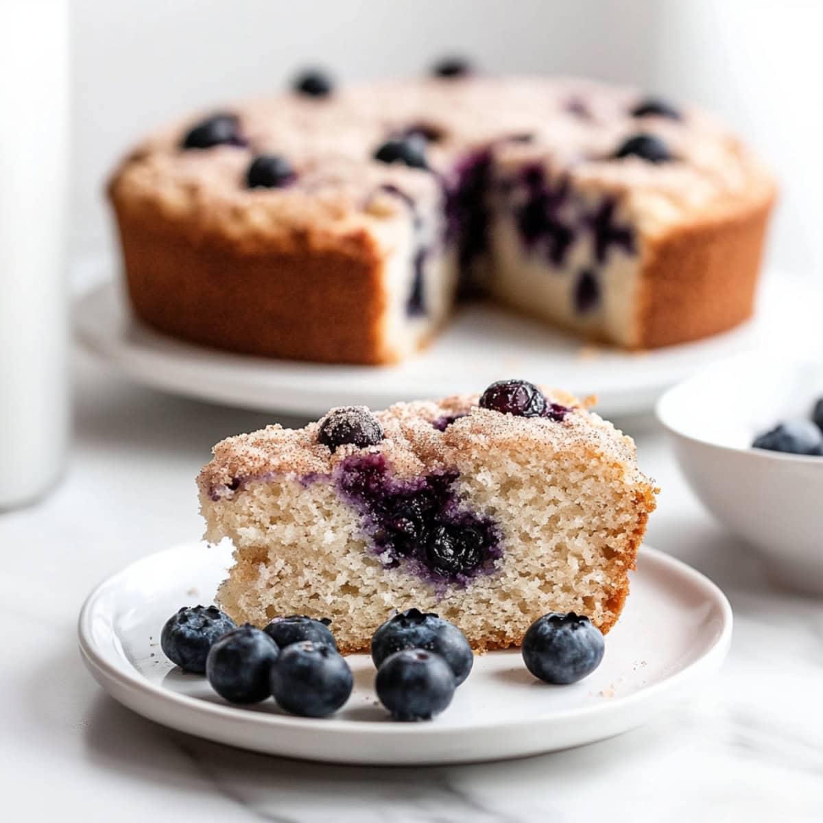 Close-up of sliced moist blueberry buttermilk cake with a golden brown crust on a plate.