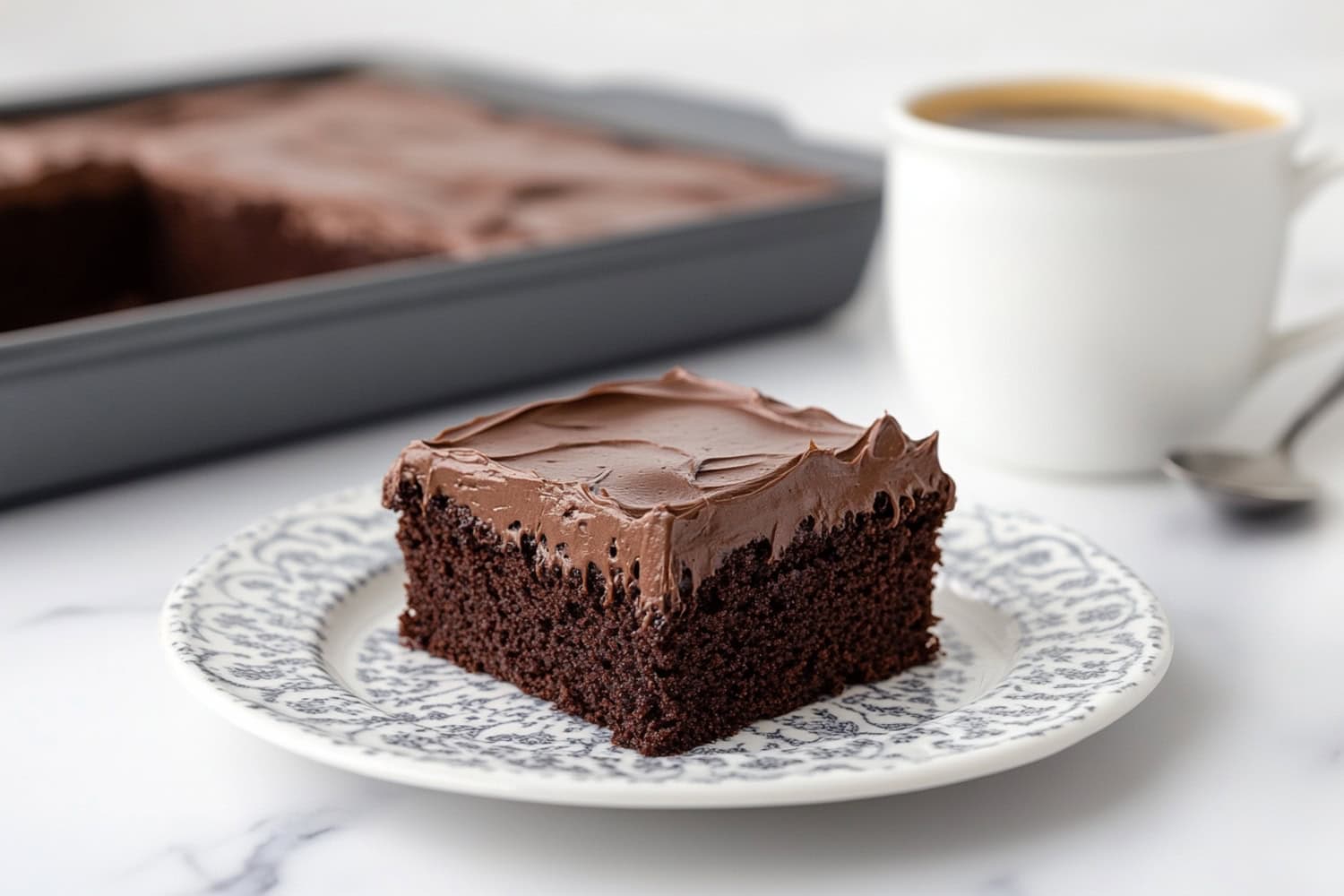 A serving of chocolate buttermilk cake with thick layers of frosting, sitting in an elegant plate.