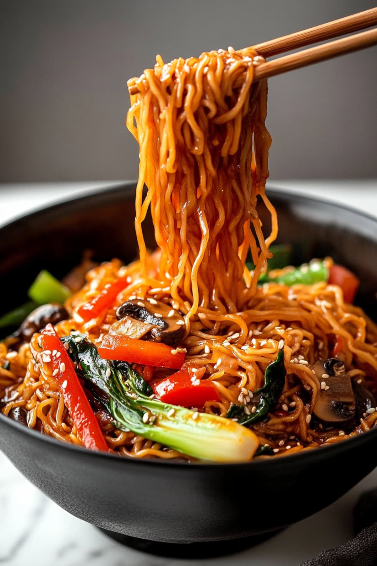 Homemade lo mein with bell peppers, bok choy and mushrooms, sprinkled with sesame seeds in a black bowl.