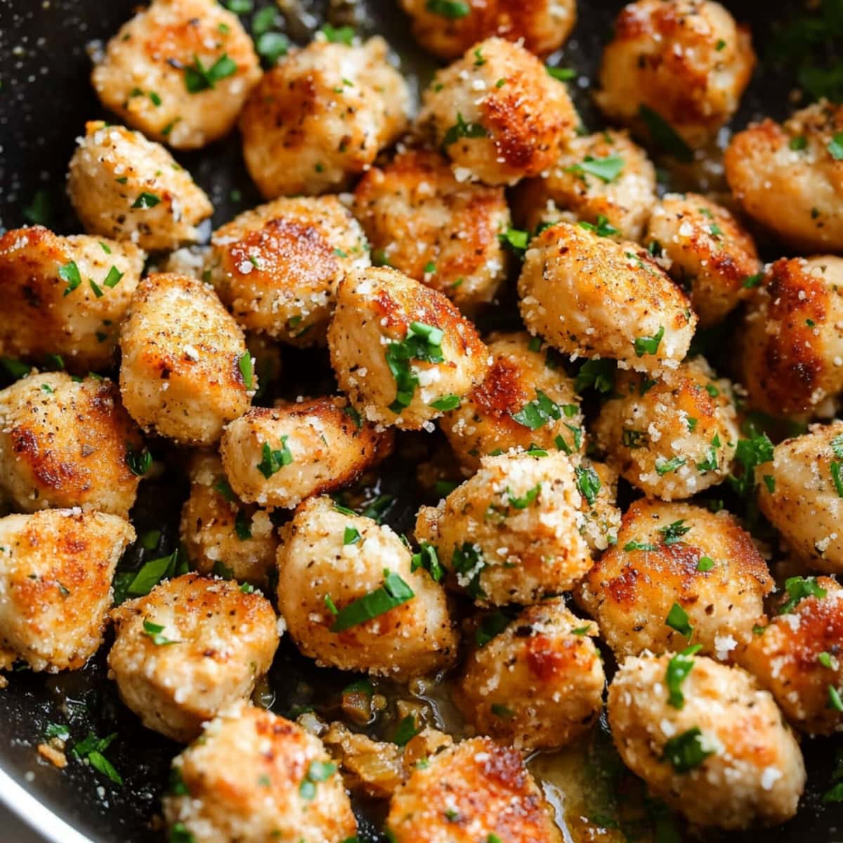 Garlic parmesan chicken bites pieces with chopped parsley in a skillet.