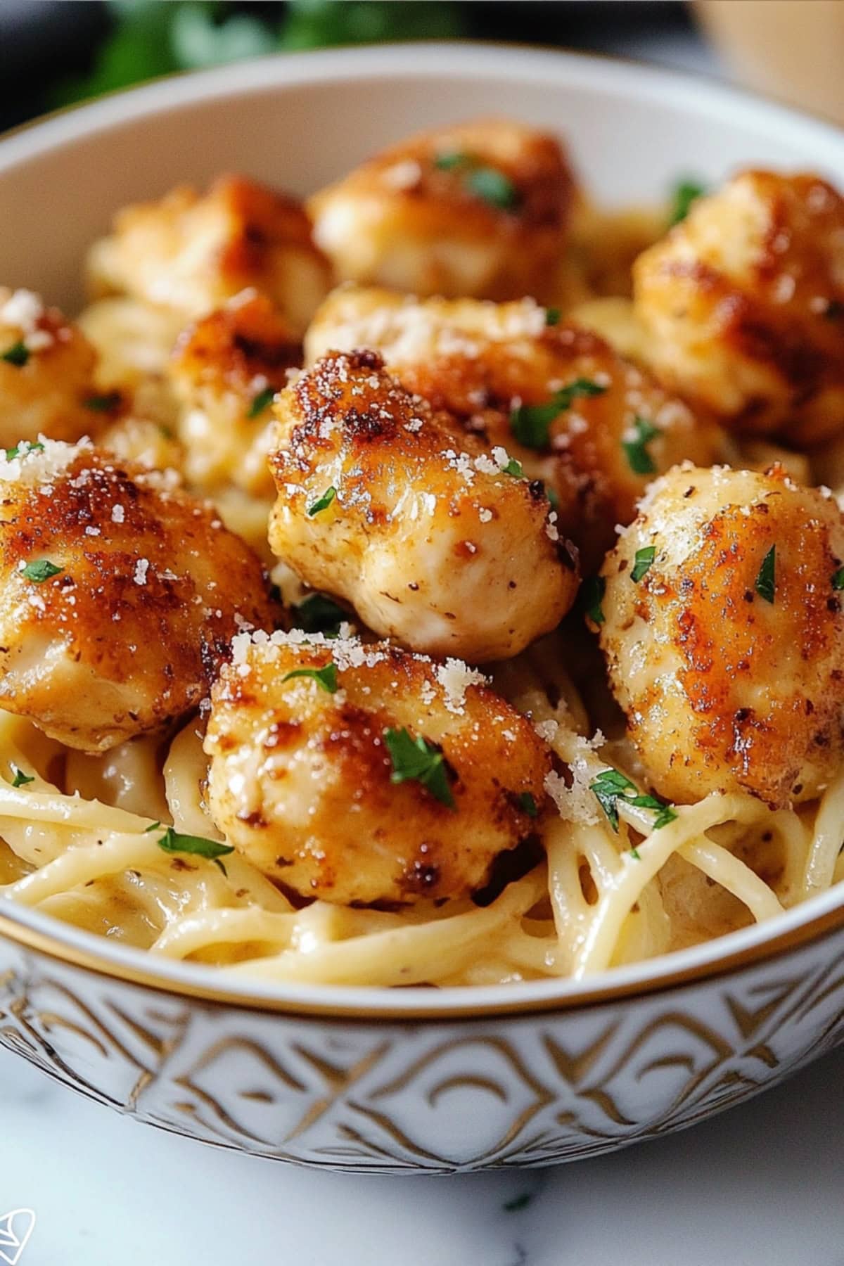 A close-up of garlic parmesan chicken bites with pasta in a bowl.