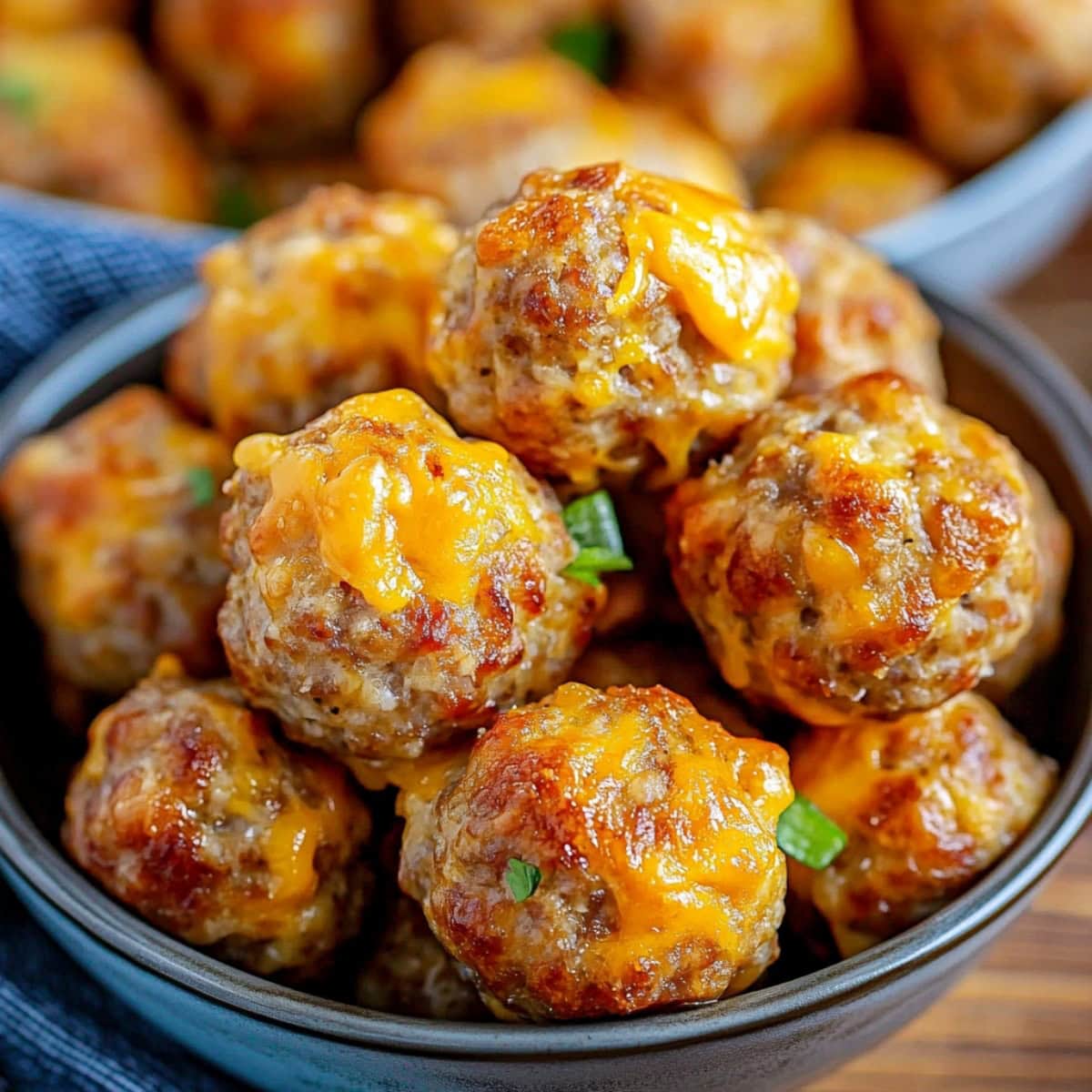Pancake sausage balls with melted cheese and a chives garnish served in a blue bowl.