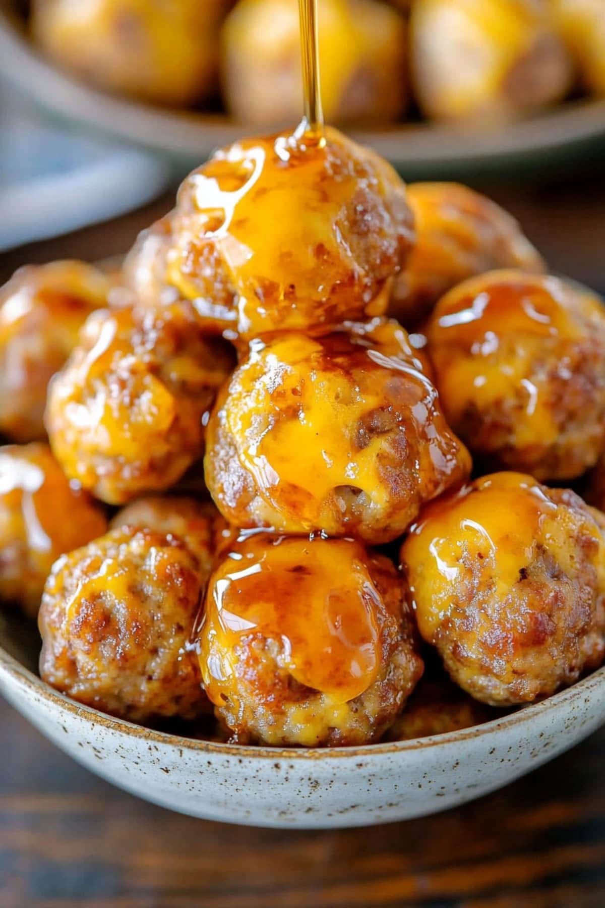 Syrup dripping over bowl of pancake sausage balls in a white bowl.