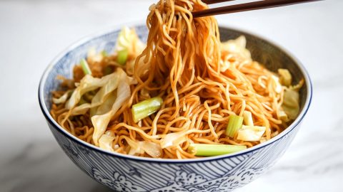 Wooden chopsticks lifting noodles from serving in a bowl.