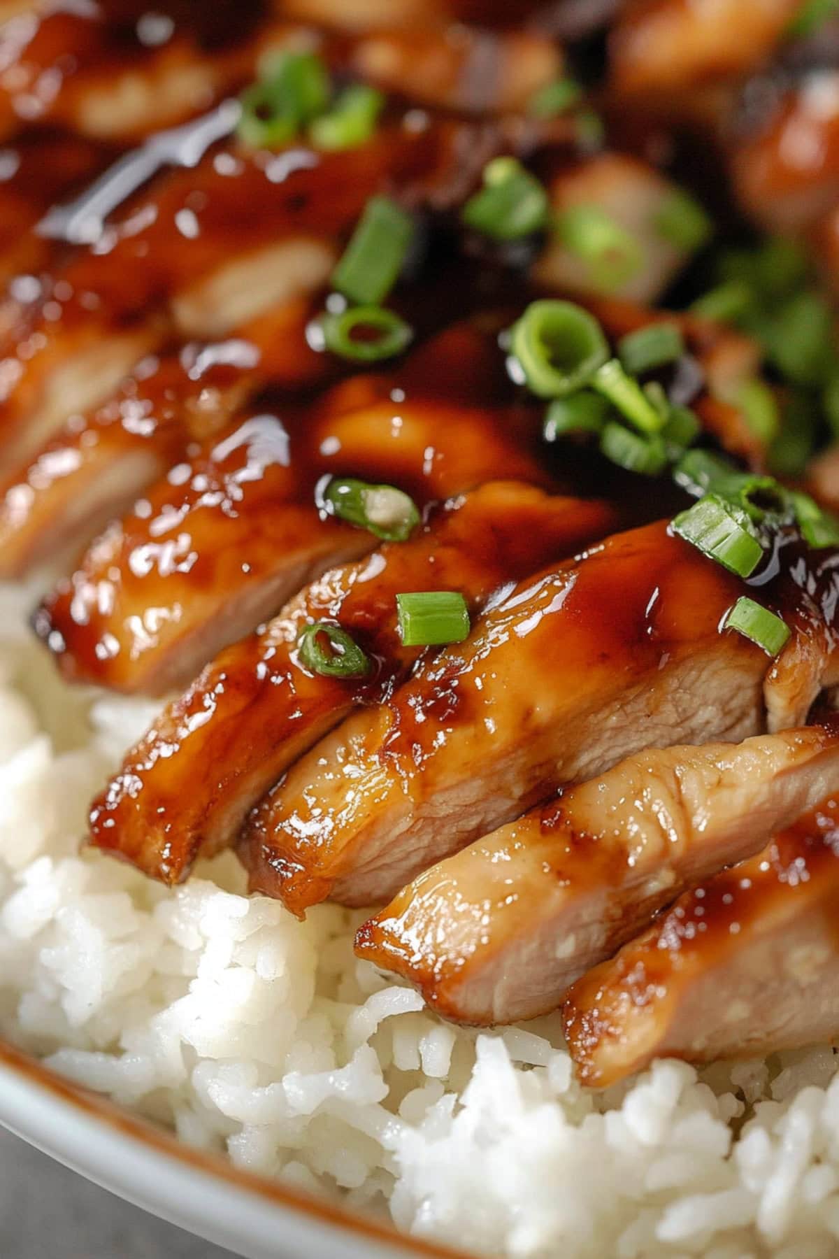 Sliced teriyaki chicken served on top of white rice in a bowl.