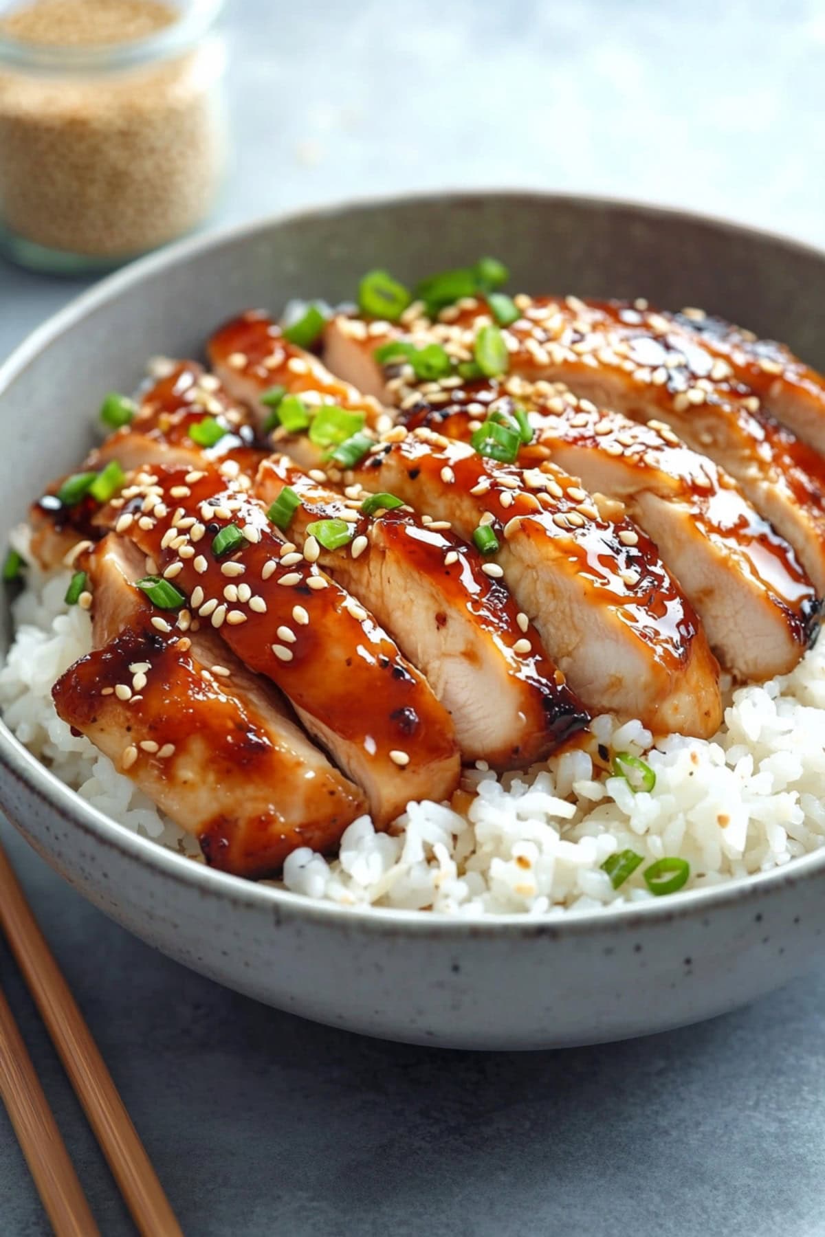 White rice in a bowl served with sliced teriyaki chicken on top.