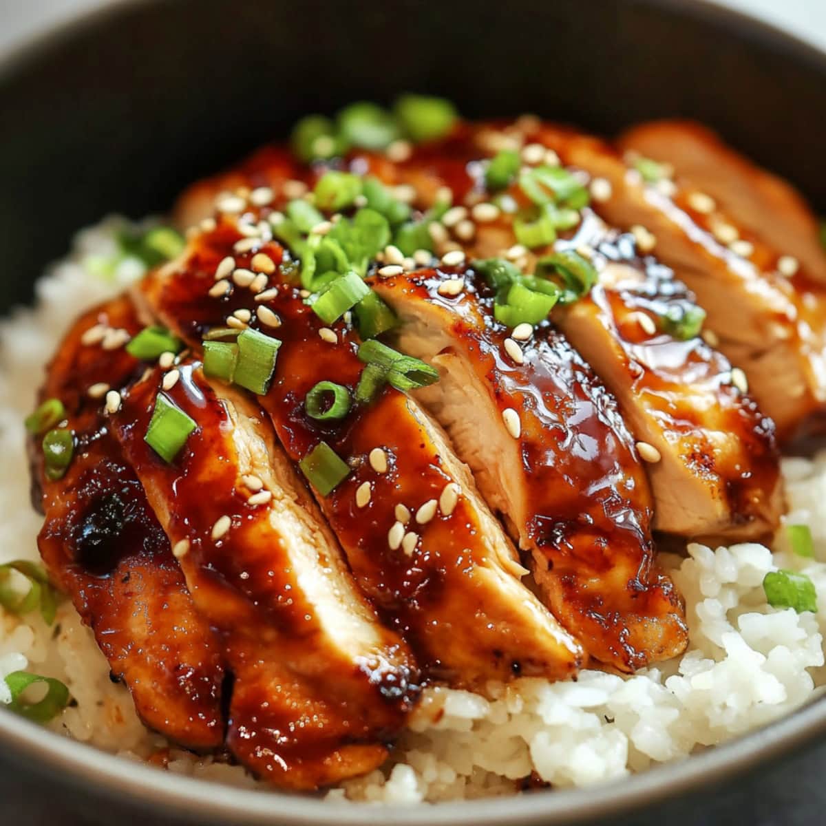 White rice in a black bowl served with sliced teriyaki chicken on top.