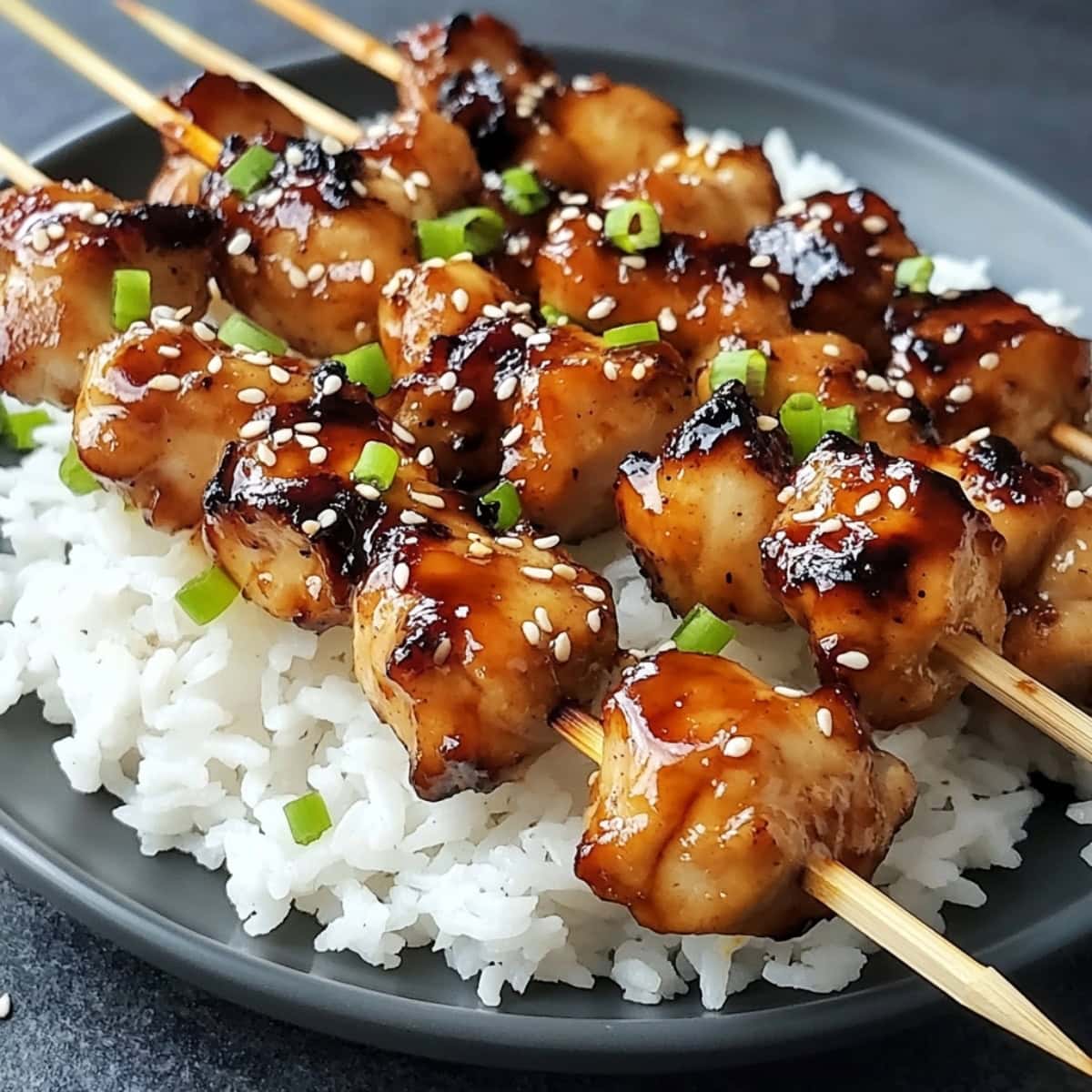 A plate of grilled chicken skewers glazed with homemade teriyaki sauce and served with steamed rice.