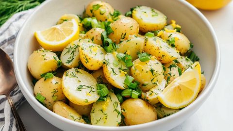 A bowl of zesty lemon potato salad with fresh dill and chopped green onions.