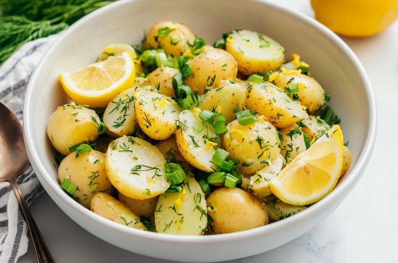 A bowl of zesty lemon potato salad with fresh dill and chopped green onions.