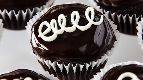 Chocolate ganache covered cupcakes decorated with swirls on top.