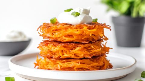 Stack of sweet potato hash in a white plate with sour cream on top.