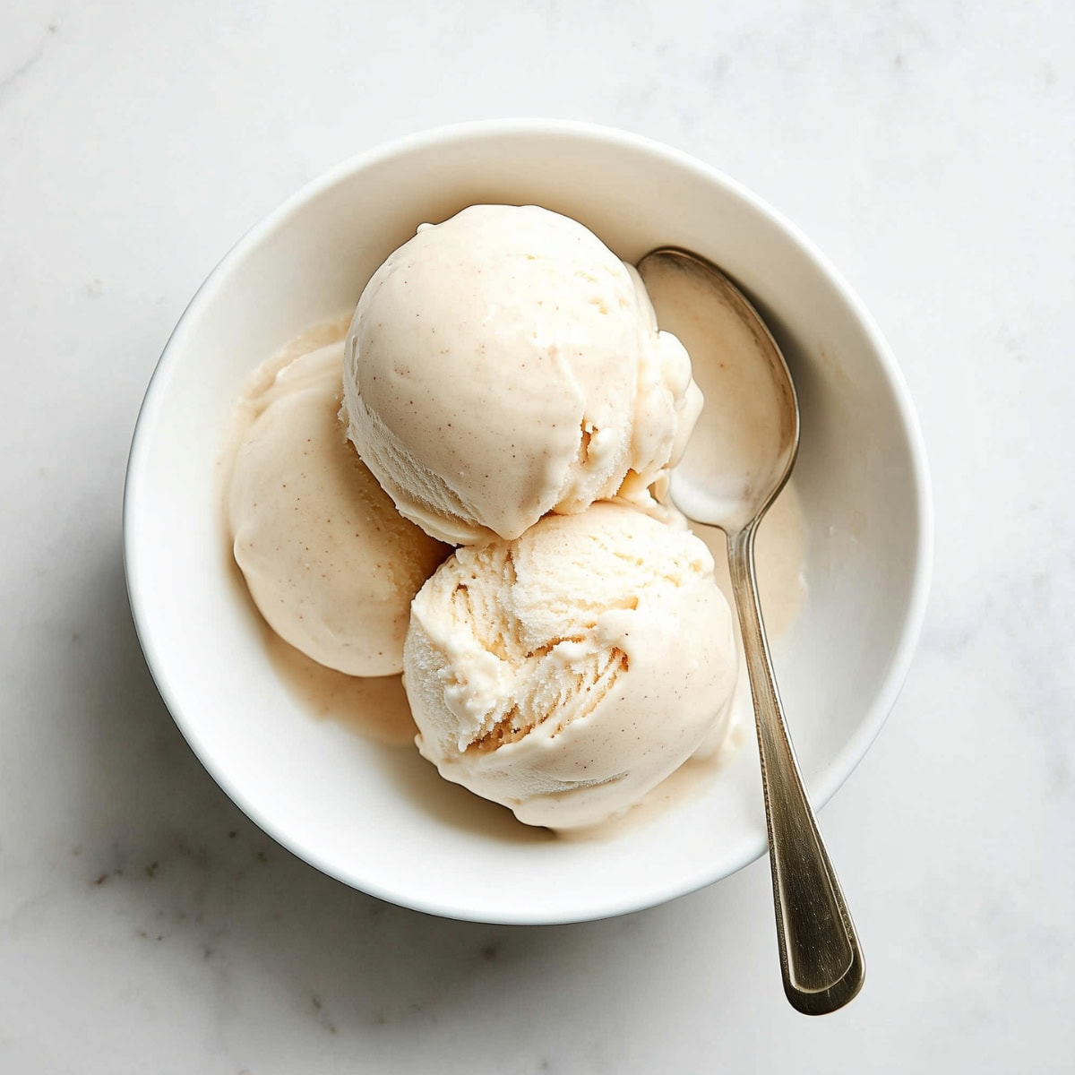 Three scoops of banana ice cream in a bowl on a white marble table.