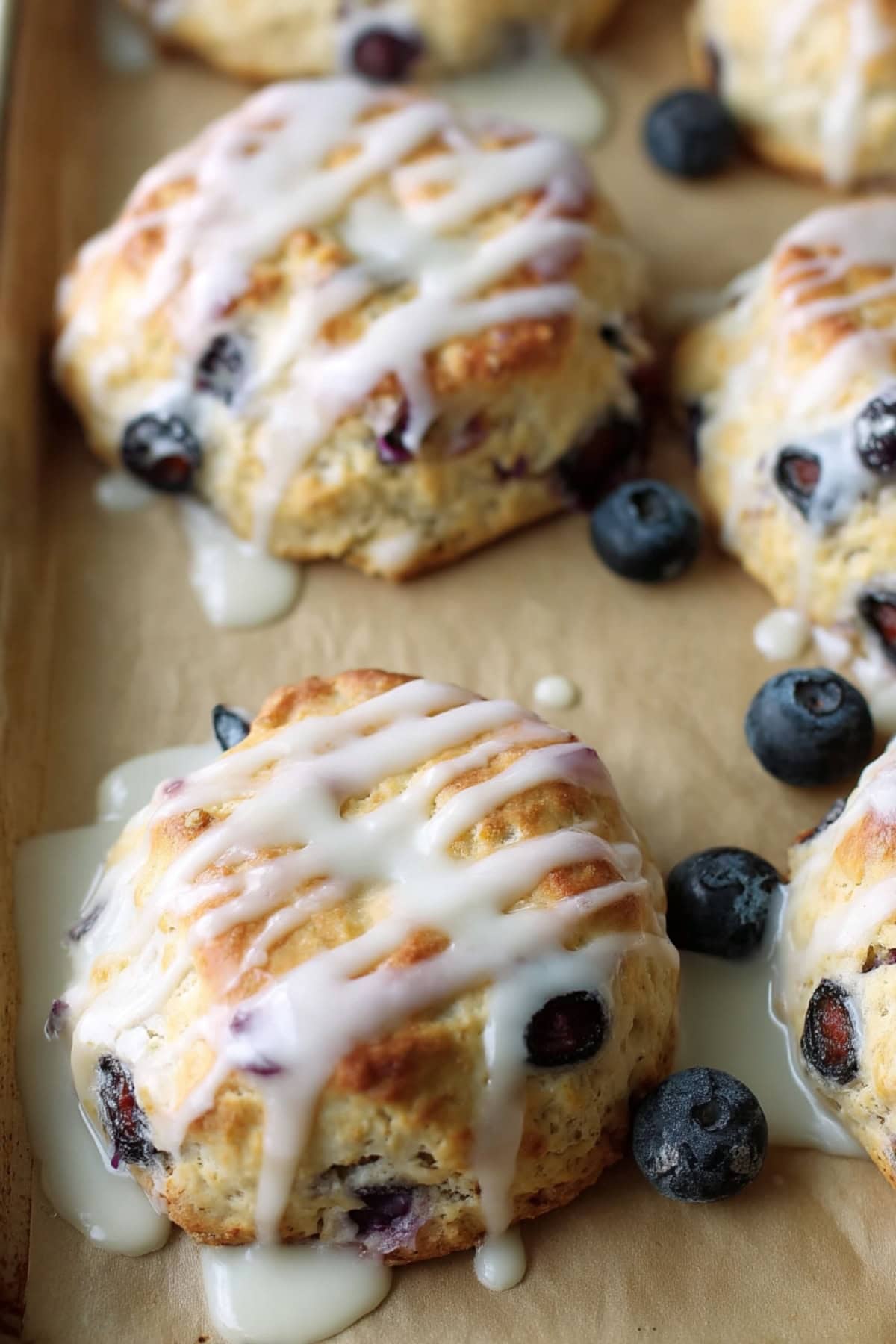 Freshly baked blueberry biscuits on parchment paper, dripping with vanilla glaze.