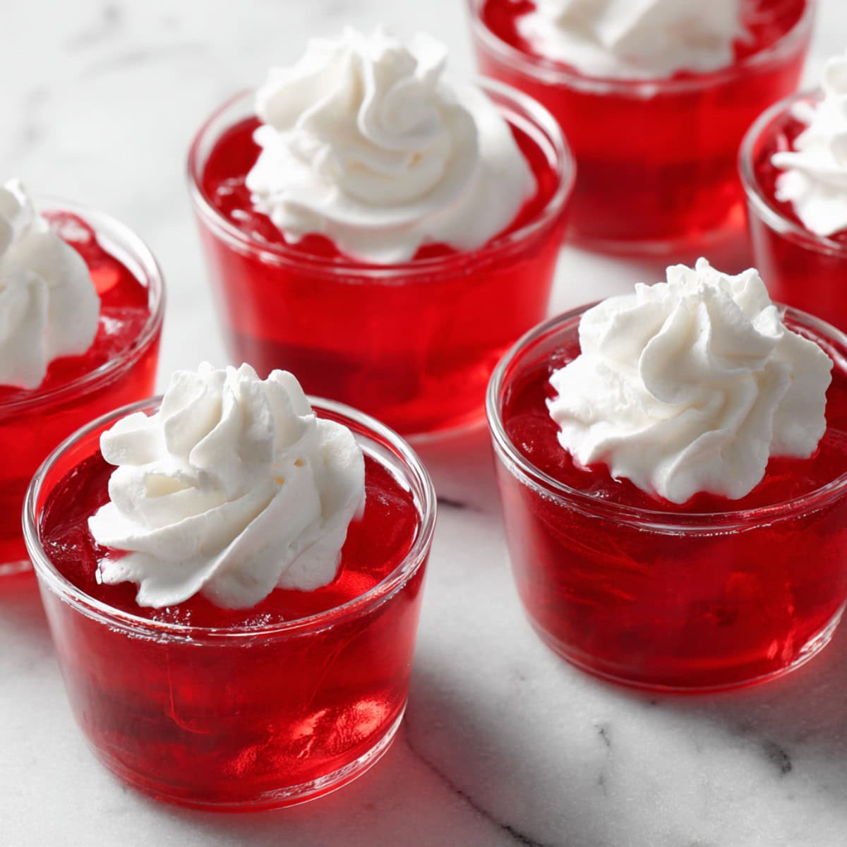 Cups of red jello with whipped cream.