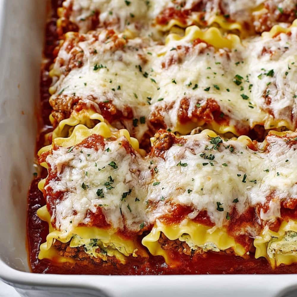 Cheesy lasagna roll ups in a baking dish.